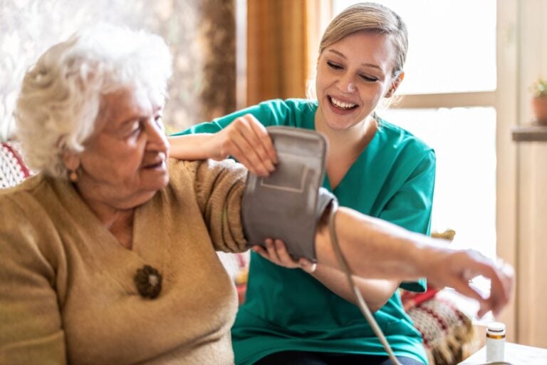 women holding out arm for blood pressure cuff test with smiling nurse in background